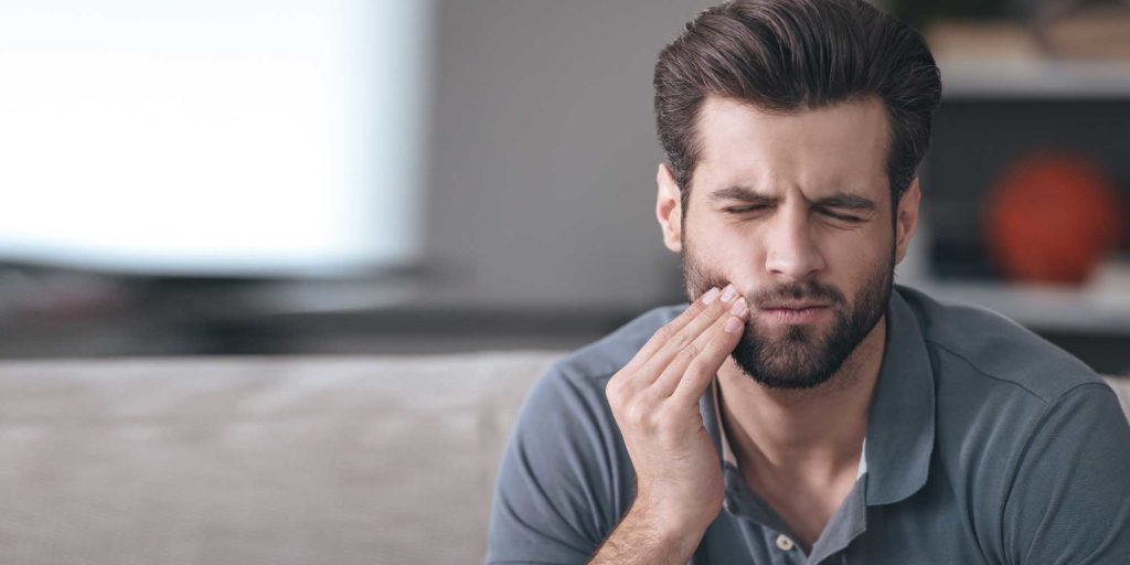 Guy holding jaw in pain at home wondering why he';s not at teeth4you implant center